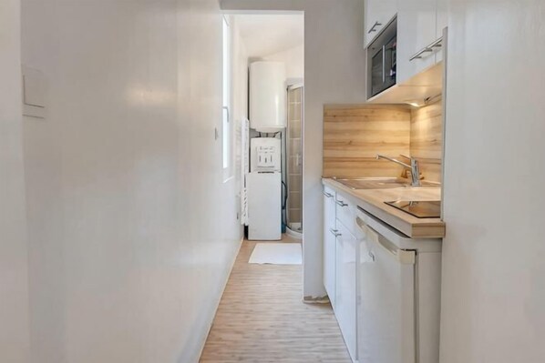 Een smalle gang die leidt naar een keuken met witte kastjes, een houten aanrecht en een spoelbak.