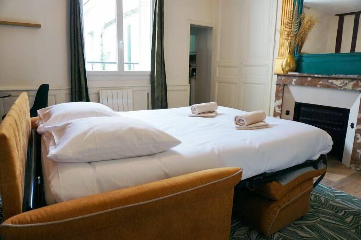A hotel room with a bed, a chair, a fireplace, and a window.