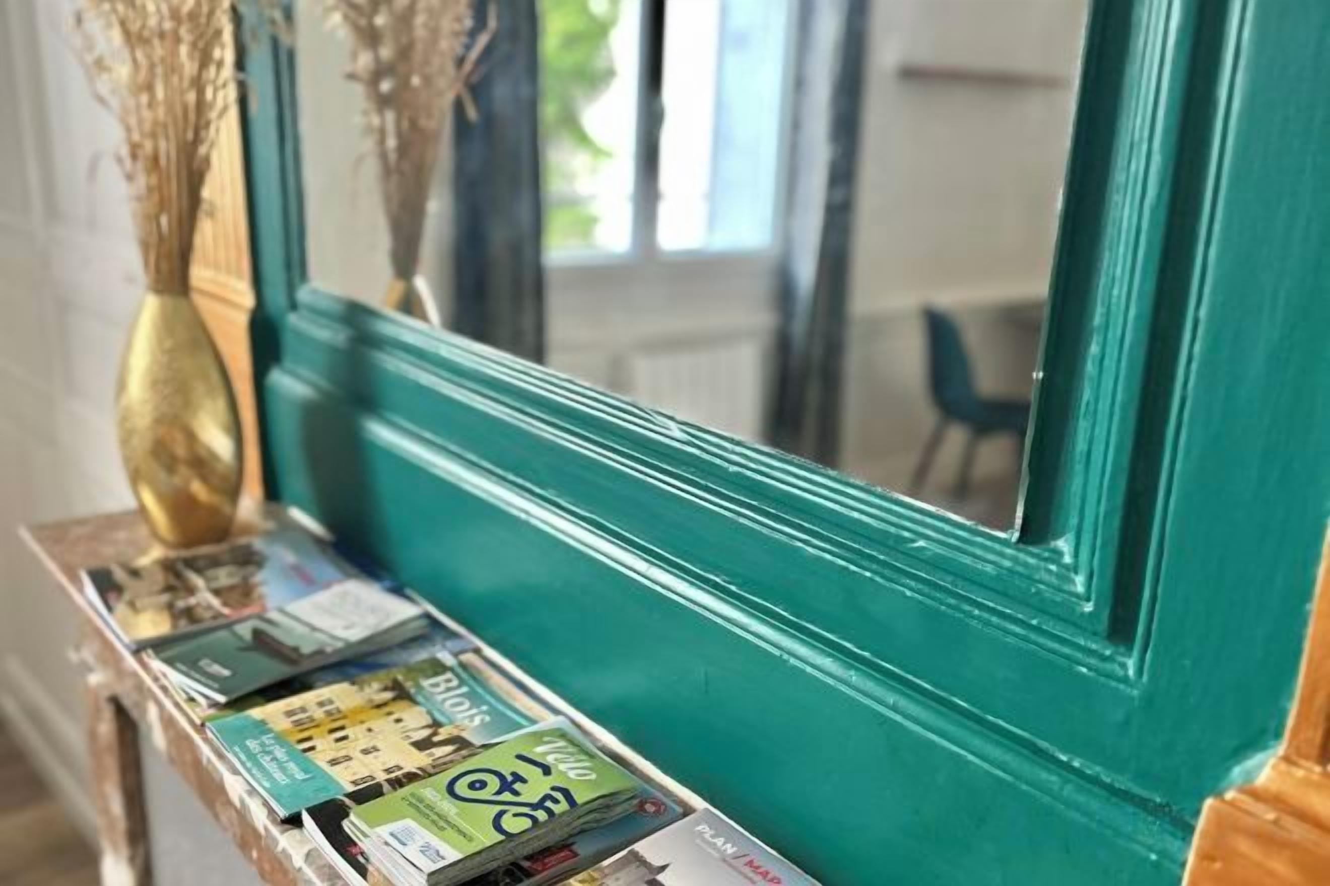 A teal painted wall with a mirror reflecting a room interior.
