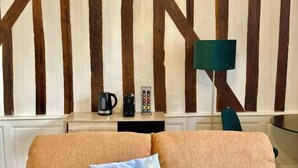 A room with a wooden wall panel design, a sofa with a cushion, a coffee maker, a kettle, a tray with cups, and a green floor lamp. - Charming studio, train station nearby (Tours)