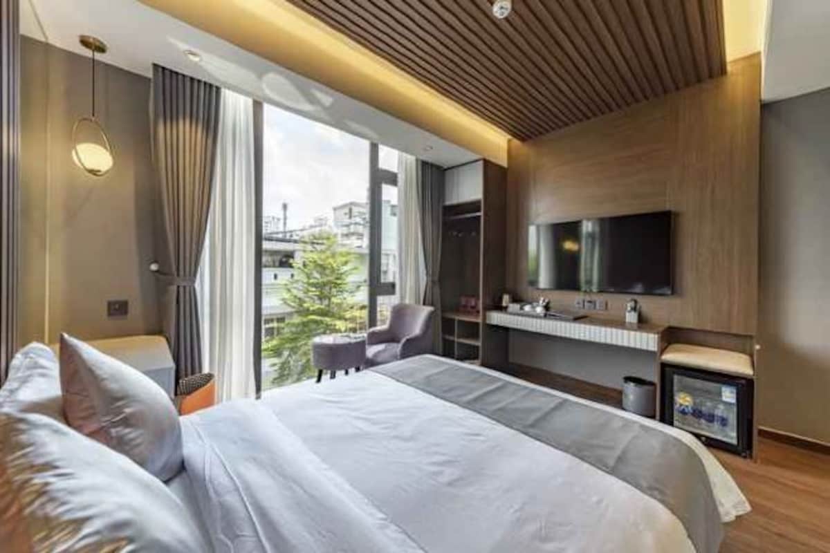 Una habitación de hotel moderna con una cama grande, televisor, un pequeño espacio de descanso y vista a la ciudad.