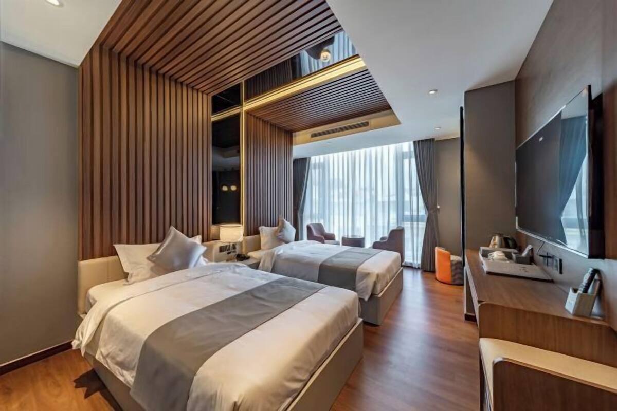 Una habitación de hotel moderna con dos camas, un televisor, un escritorio y un ventanal grande.