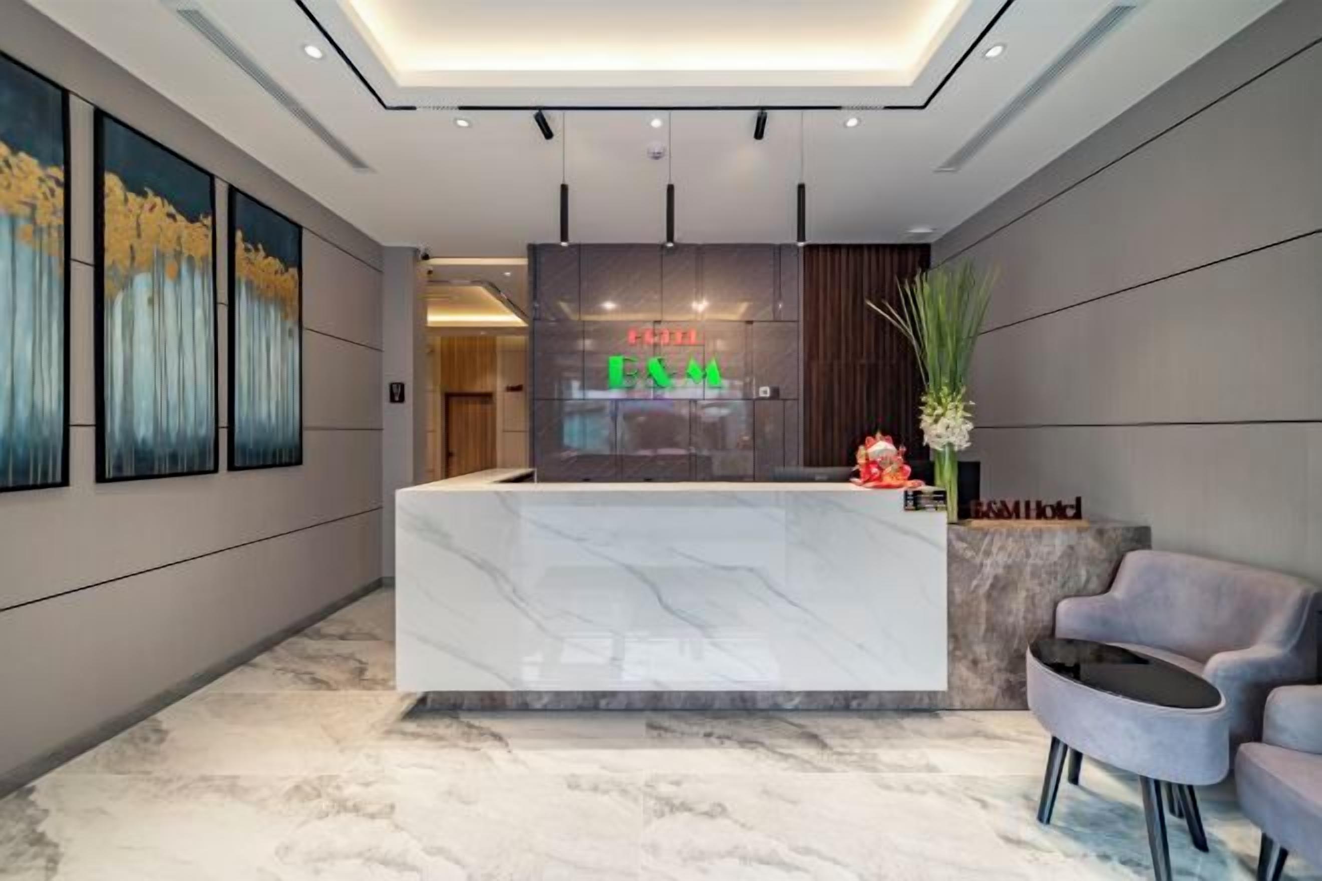 A hotel reception area with a marble reception desk, a seating area with a grey sofa, and framed artwork on the walls.