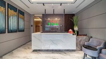 A hotel reception area with a marble reception desk, a seating area with a grey sofa, and framed artwork on the walls.