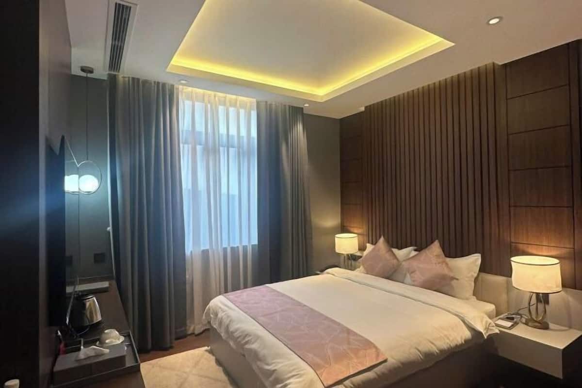 Una habitación de hotel moderna con una cama grande, lámparas de noche, un televisor de pantalla plana y una lámpara en el techo.