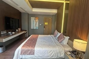 A hotel room with a bed, bedside table, lamp, TV, and a desk with a mirror and toiletries. - B&M HOTEL (Ho Chi Minh City)