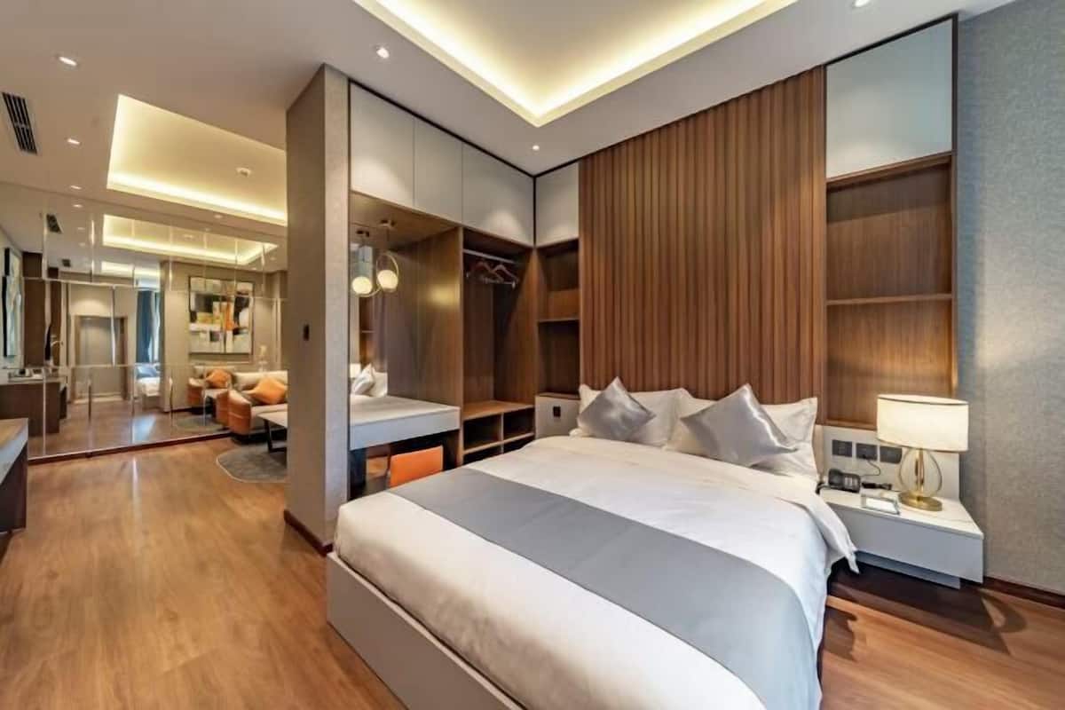 Una habitación de hotel moderna con una cama grande, armario empotrado y zona de estar con sofá y sillones.