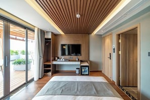 Un dormitorio moderno con una cama grande, un escritorio empotrado, televisión y puerta corrediza de vidrio a un balcón.