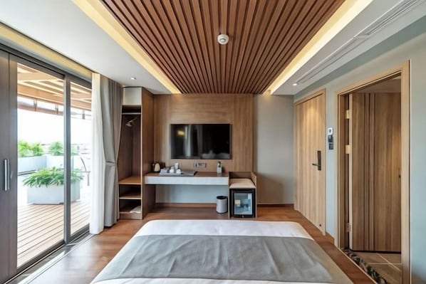 A modern bedroom with a large bed, a built-in TV, a wooden ceiling, and a sliding glass door to a balcony.