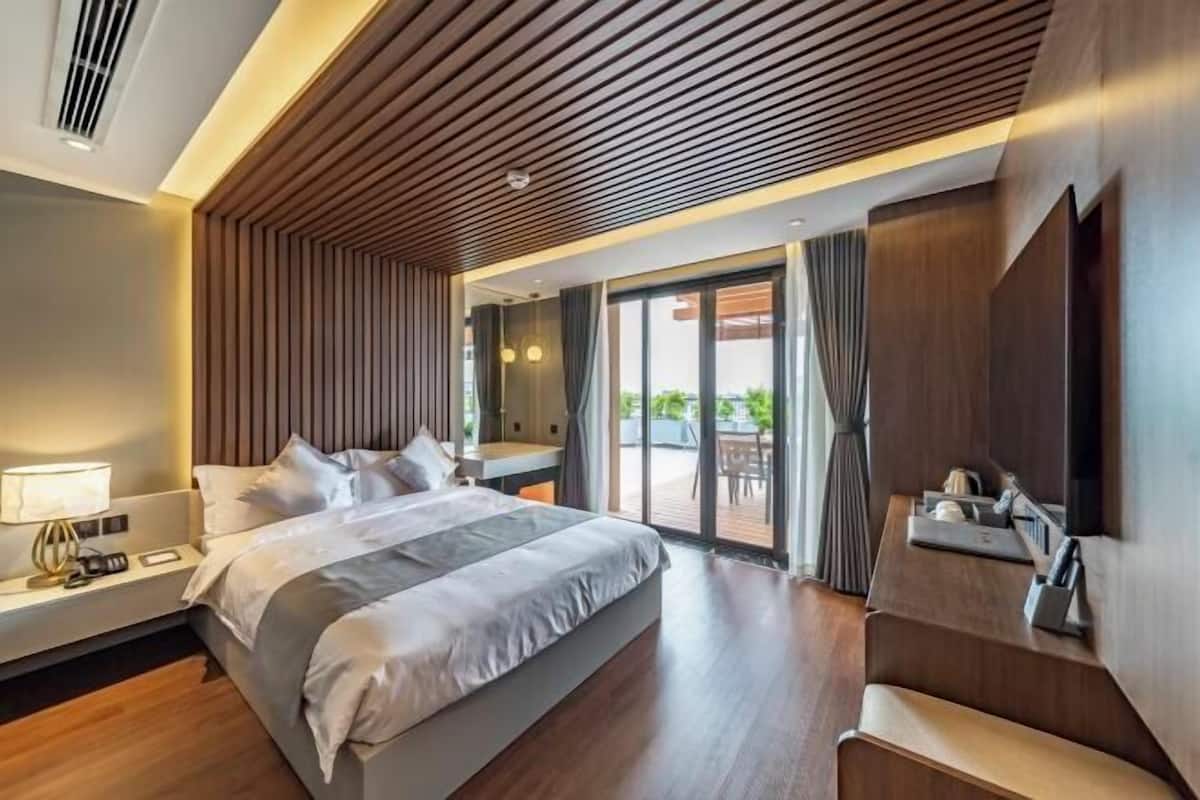 Habitación de hotel moderna con una cama grande, un escritorio con lámpara, televisor y puerta corrediza de vidrio que da a un espacio exterior.