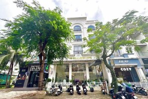 A hotel with a central entrance, a parking area with motorcycles, and a tree in the foreground. - The Shilla Hotel Phu My Hung (Ho Chi Minh City)