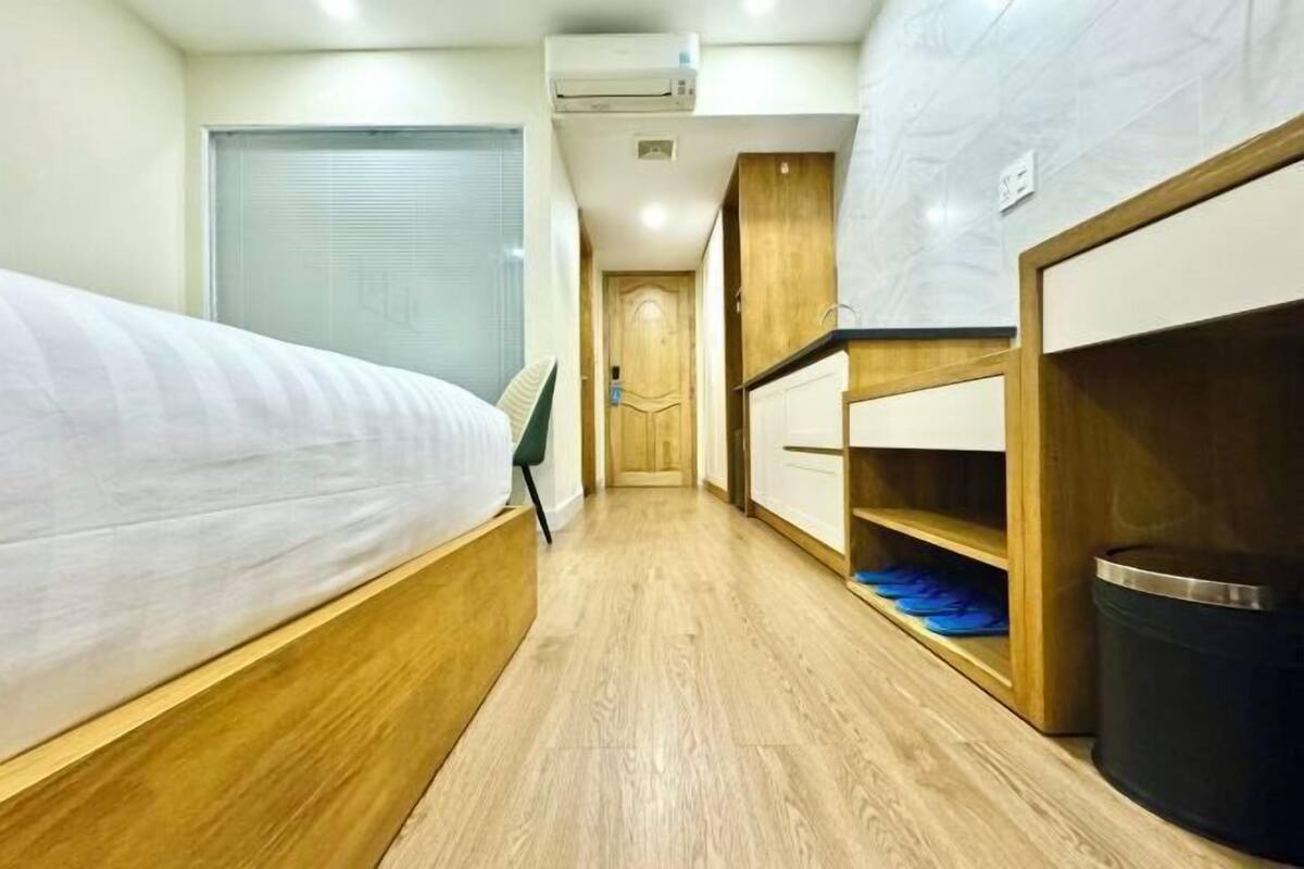Un corridoio stretto con un letto a sinistra, mensole di legno a destra e una porta in fondo.