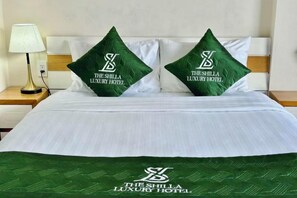Ein Bett mit weißer Bettdecke und zwei grünen Kopfkissen mit dem Hotel-Logo.