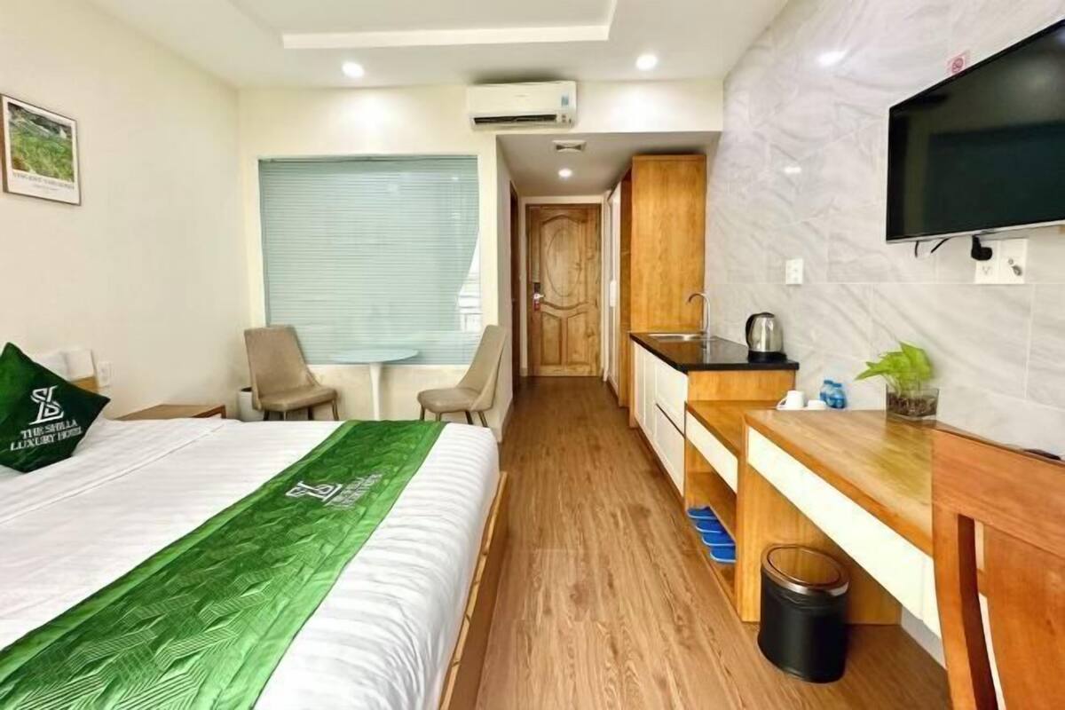 Una camera d'albergo compatta con un letto, una piccola scrivania, un angolo cottura e una TV a parete.