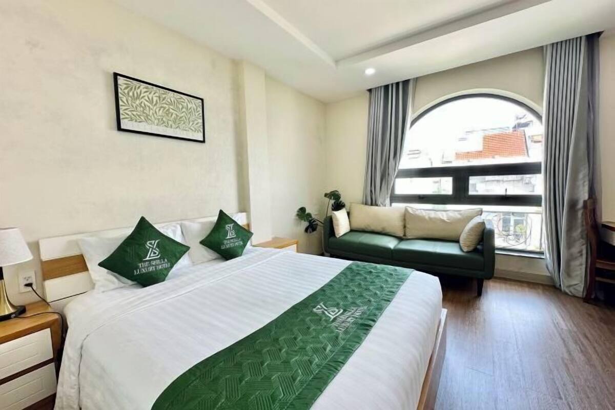 Una camera d'albergo con un letto grande, un divano verde, una finestra con tende e un quadro appeso al muro.