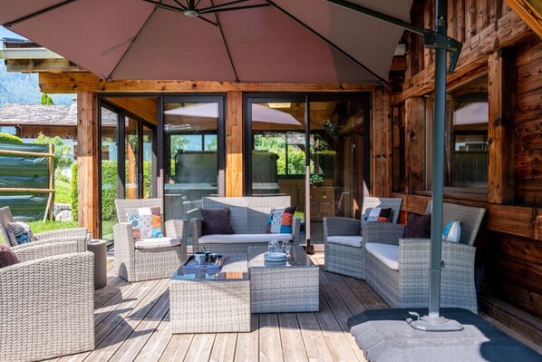 A wooden deck with wicker furniture and umbrellas, overlooking a garden.