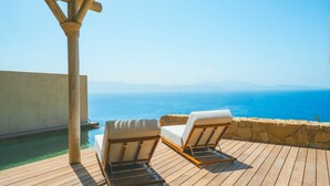 A wooden deck with two lounge chairs overlooking a pool and the sea.