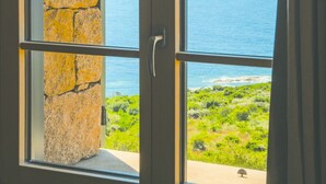 A view through a window with a stone wall, a clear sky, and the sea.