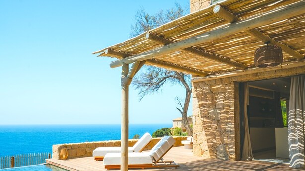 A poolside area with lounge chairs, a pergola, and a view of the sea.