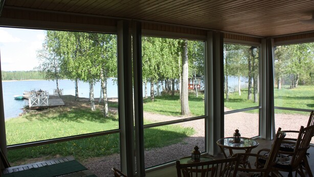 A room with large windows overlooking a lake, furnished with chairs and a small table. - Cottage Baydar (Kouvola)