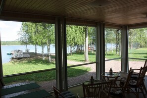 A room with large windows overlooking a lake, furnished with chairs and a small table. - Cottage Baydar (Kouvola)