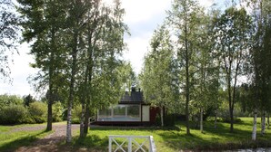 A wooden deck leading to a glass-walled cabin surrounded by trees. - Cottage Baydar (Kouvola)
