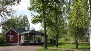 A red cabin with a glass extension, surrounded by trees and a gravel path. - Cottage Baydar (Kouvola)