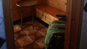A wooden cabin room with a window, a small table, a bench, and a green bag. - Cottage Baydar (Kouvola)