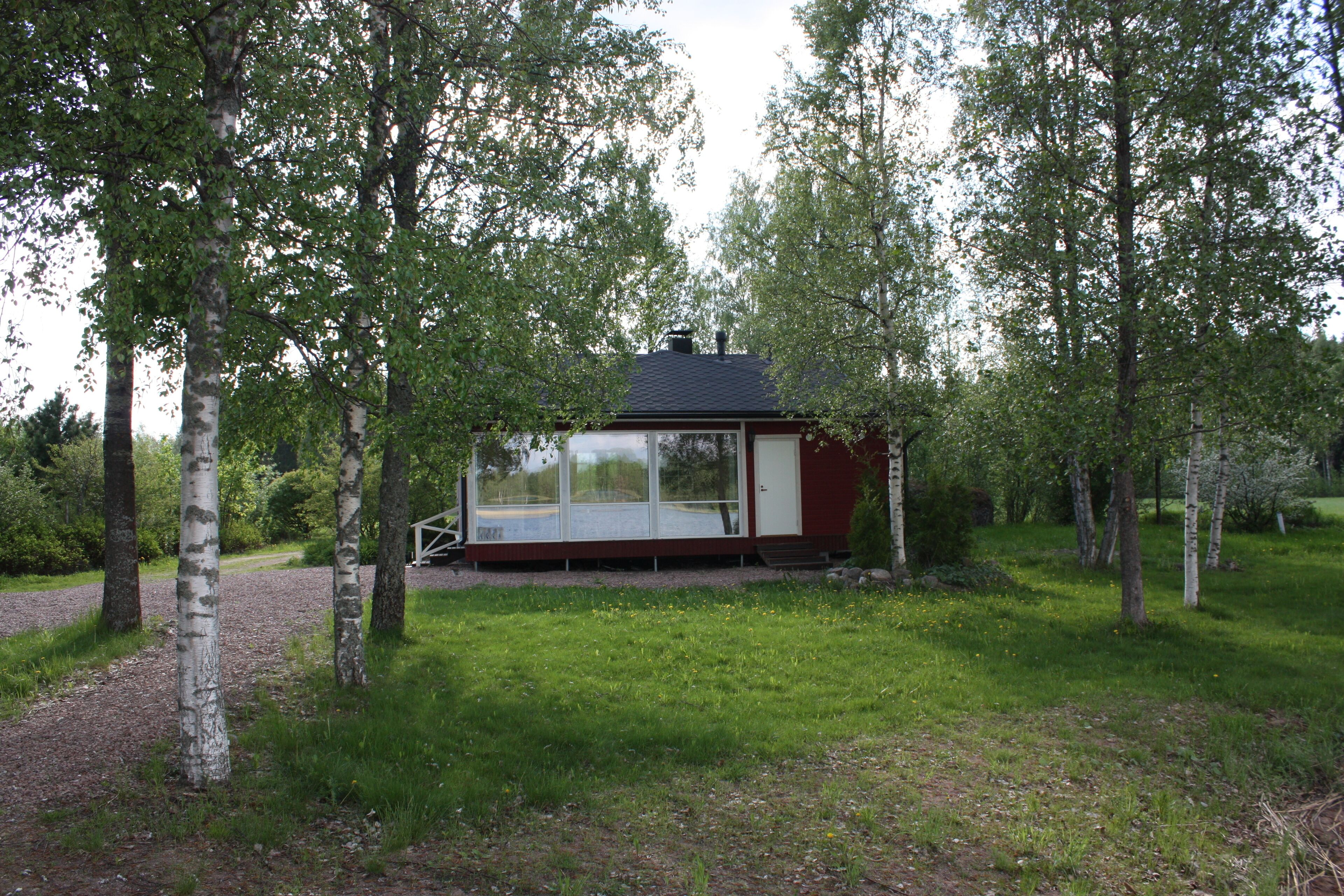 A small cabin with a glass door and windows, surrounded by trees and grass.
