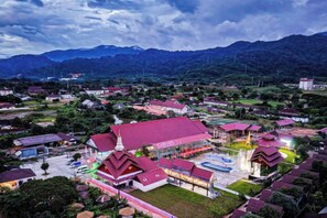 A large building with a red roof, surrounded by smaller structures and greenery, with mountains in the background. - Hometown of Dragon Hotel (Vang Vieng)