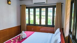 Una habitación de hotel con cama, ventana con cortinas, unidad de aire acondicionado y lámpara fijada a la pared.