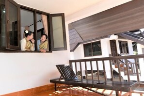 A balcony with a black metal railing, a black lounge chair, and a window with a view of a building. - Hometown of Dragon Hotel (Vang Vieng)