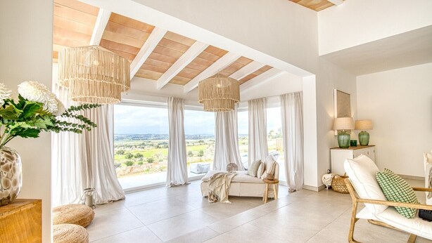 A spacious room with a large window, a sofa, a chair, and a lamp.