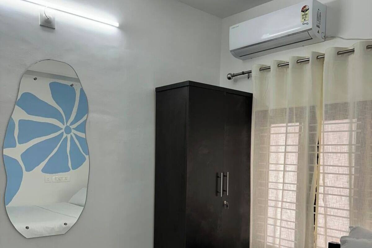 Una camera da letto con un letto, un armadio, un condizionatore d'aria a muro, una luce a soffitto e una finestra con tende leggere.