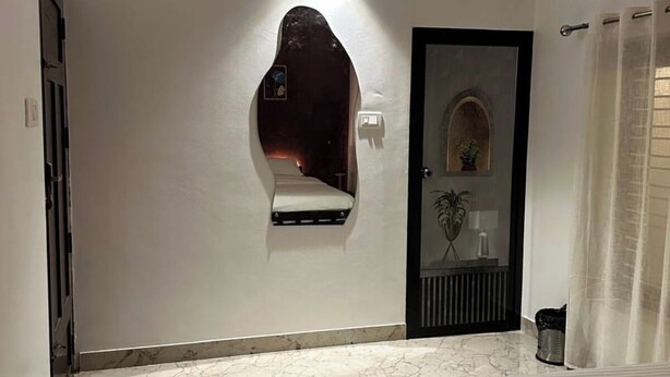Ein Schlafzimmer mit einem Bett, einem an der Wand befestigten Regal, einer Tür mit Spiegel und einem Deckenventilator.