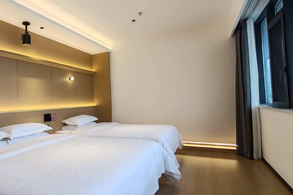 Ein modernes Hotelzimmer mit einem großen Bett, Nachttischen und einem großen Fenster mit Vorhängen.