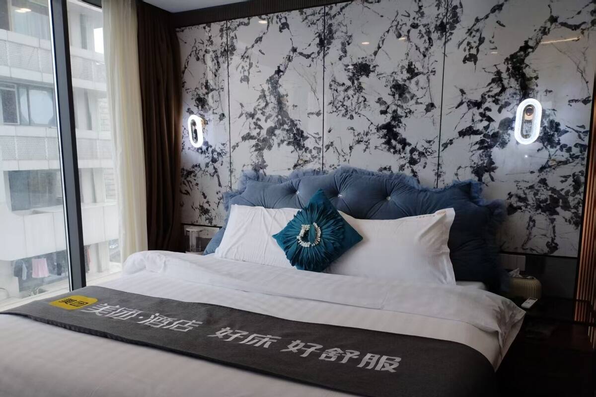 Ein Hotelzimmer mit einem grossen Bett, einem Kopfteil im Marmor-Design und Blick auf die Stadt durch grosse Fenster.