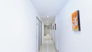 A corridor with white walls, a door on the left, and a framed artwork on the right. - Mitr Inn Nimman (Chiang Mai)
