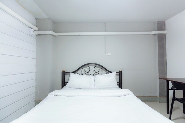 A single bed with white bedding, a metal headboard, and a small table to the right.