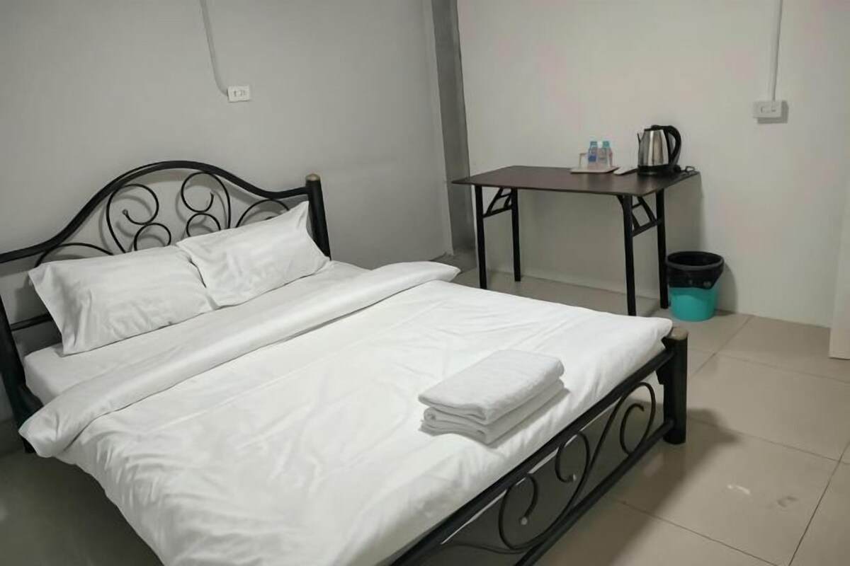 A bed with white linens, a metal frame, and a table with a kettle and cups beside it.