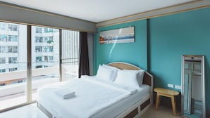 A modern hotel room with a large bed, a small bedside table, a painting on the wall, and a view of a cityscape through large windows. - Mitr Inn Nimman (Chiang Mai)