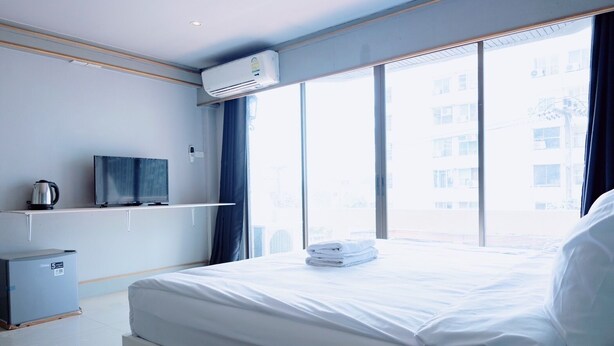 A hotel room with a bed, a television, a kettle, and a window with a view of buildings. - Mitr Inn Nimman (Chiang Mai)