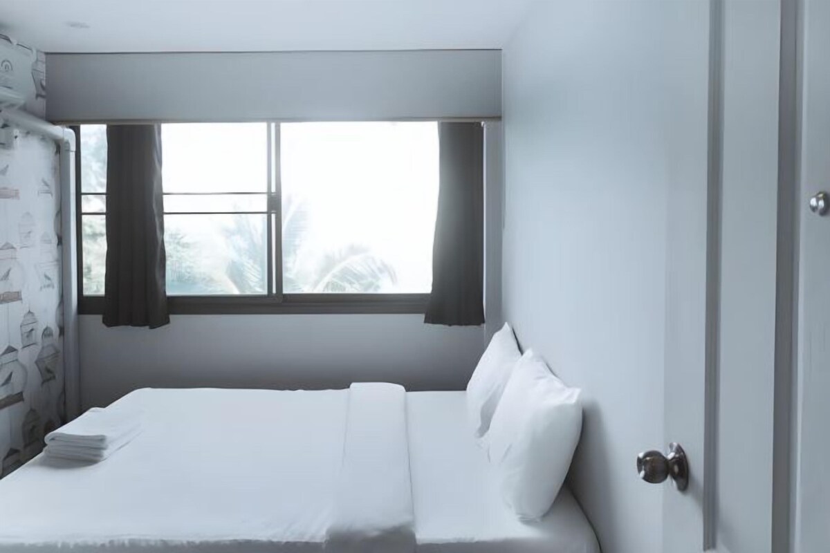 A single-bed room with a window, curtains, and a door.