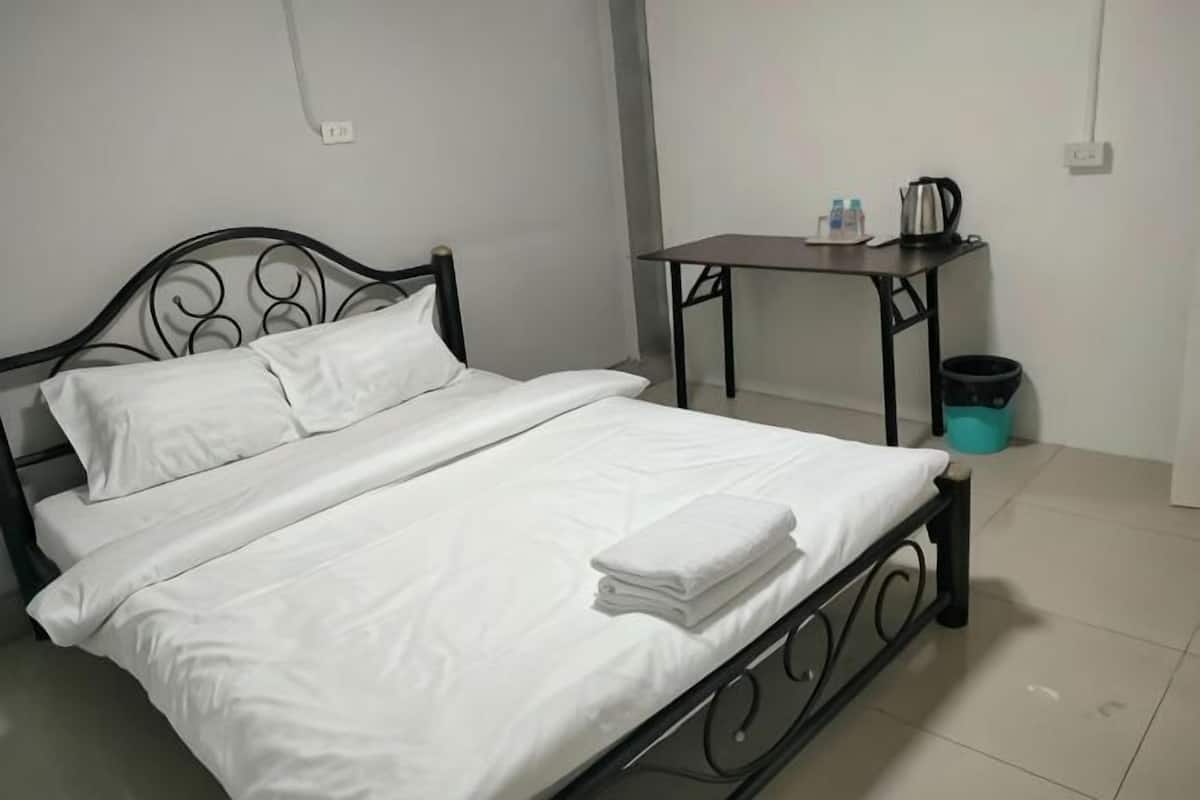A bed with white linens, a metal frame, and a table with a kettle and cups beside it.