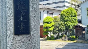 Monument de pedra amb caràcters japonesos, un pati pavimentat i edificis tradicionals al fons.