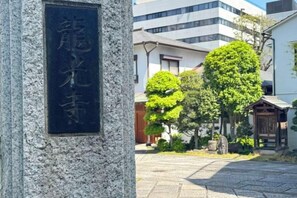 Un monumento de piedra con caracteres japoneses, un patio empedrado y edificios tradicionales al fondo.