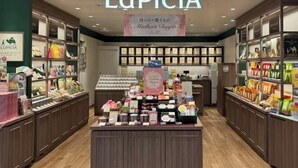A store interior with shelves stocked with various products, a prominent display case in the center, and a sign above reading "LUPICIA". - Tokyo Sakura Hotel (Tokyo)