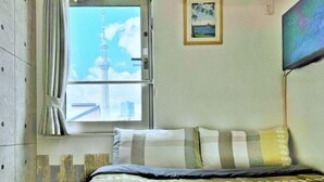 A hotel room with a bed, a window with a view of a tower, a framed picture on the wall, and a television mounted on the wall. - Tokyo Sakura Hotel (Tokyo)