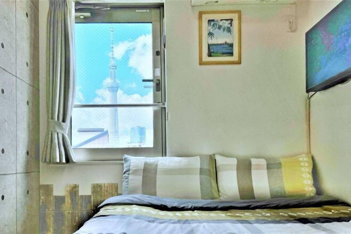 A hotel room with a bed, a window with a view of a tower, a framed picture on the wall, and a television mounted on the wall.