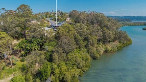 A coastal property with a prominent sign for Holiday Management Co., surrounded by lush greenery and a clear view of the sea. - Hillcrest Retreat with River Views (Tweed Heads South)